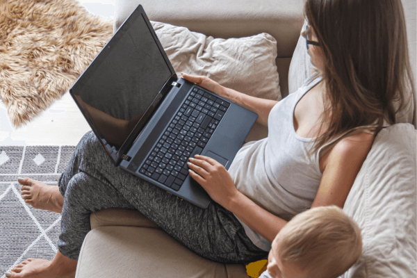赤ちゃんの横でソファに座りパソコンを開くママ